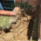 A deep trench dug around a basement window well, exposing pipes and cables for repair or installation.
